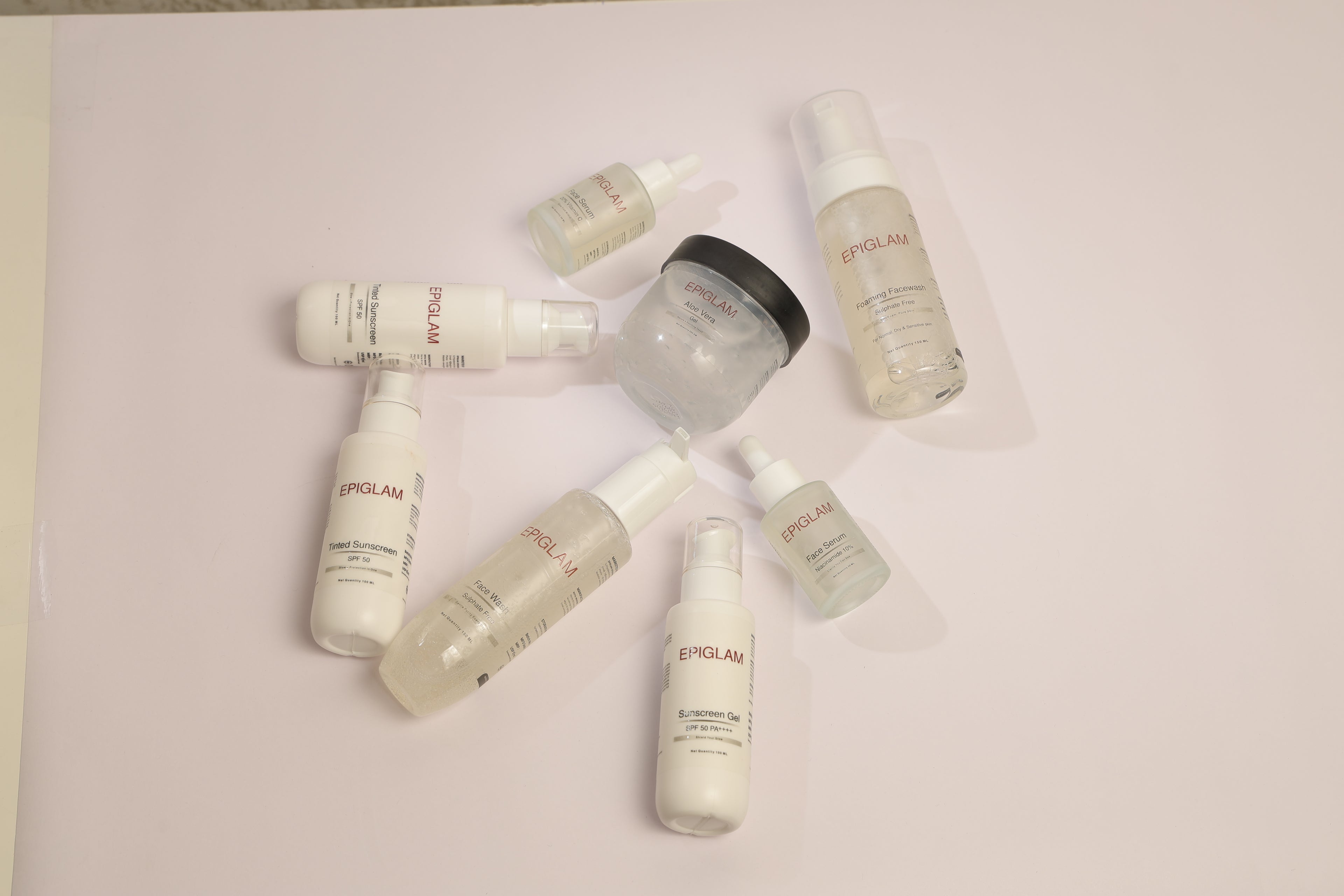 Top-down view of multiple Epiglam skincare products, including face serums, face wash, foaming cleanser, sunscreen, and aloe vera gel, arranged in a creative circle on a light background.